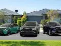 Trzy modele Toyota SUV: zielony kombi, ciemnozielony Highlander Hybrid i granatowy RAV4 Plug-in Hybrid, zaparkowane przed domami.