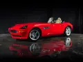 Czerwony kabriolet BMW Z8 z beżowym wnętrzem, lśniący na mokrej podłodze, odbija się w tafli wody.