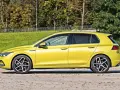 Żółty hatchback Volkswagen Golf VIII z przyciemnianymi szybami stoi na tle zieleni i drzew.