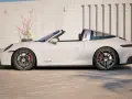 Białe Porsche 911 Targa z napisem "E-hybrid" na progu, zaparkowane przed ceglanym murem.