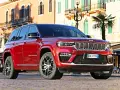 Czerwony Jeep Grand Cherokee zaparkowany na brukowanej ulicy przed budynkami z balkonami.