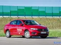 Czerwony fiat tipo sedan z napisem "Przetestuj Tipo" na drzwiach, zaparkowany na tle zielonego ekranu dźwiękochłonnego.