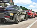 Czarny Porsche GT3 RS z numerem 3 i logo Manthey na skrzydle, gotowy do wyścigu obok czerwonych samochodów.