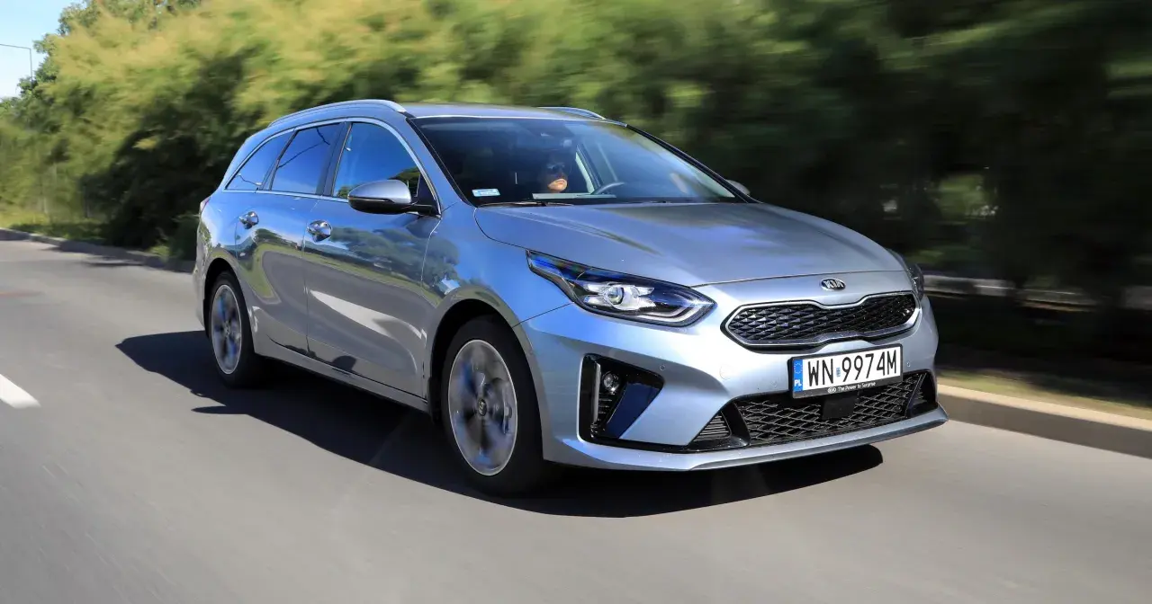 Srebrny Kia Ceed 1.6 benzyna w wersji kombi pędzi po drodze, otoczony zielenią.