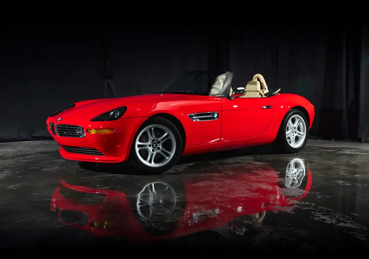 Czerwony kabriolet BMW Z8 z beżowym wnętrzem, lśniący na mokrej podłodze, odbija się w tafli wody.