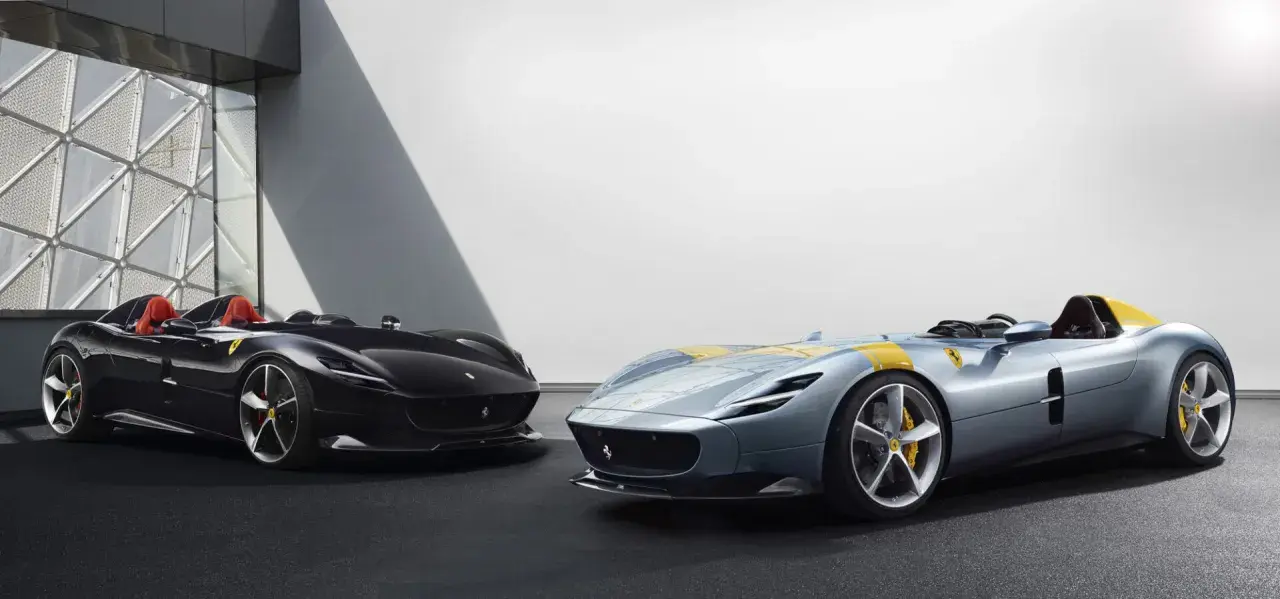 Dwa sportowe samochody Ferrari Monza SP2, jeden czarny, drugi błękitny z żółtymi pasami, prezentują swoje aerodynamiczne kształty.