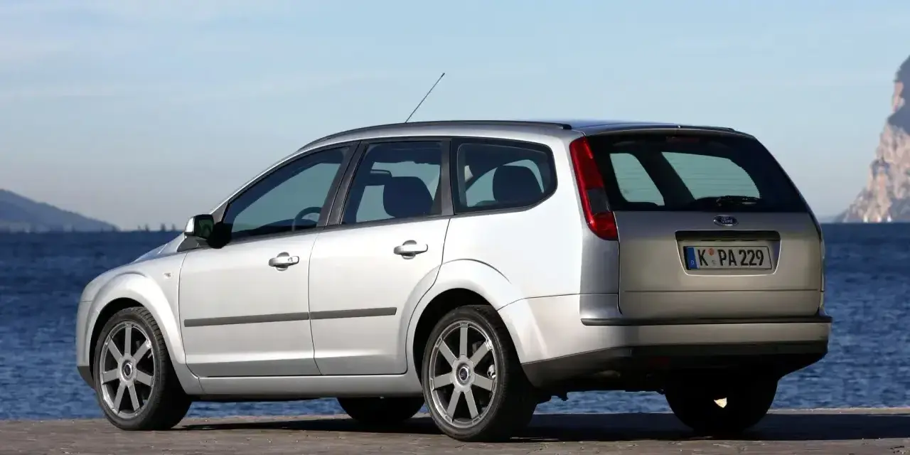 Srebrny Ford Focus MK2 1.6 benzyna kombi zaparkowany nad wodą.