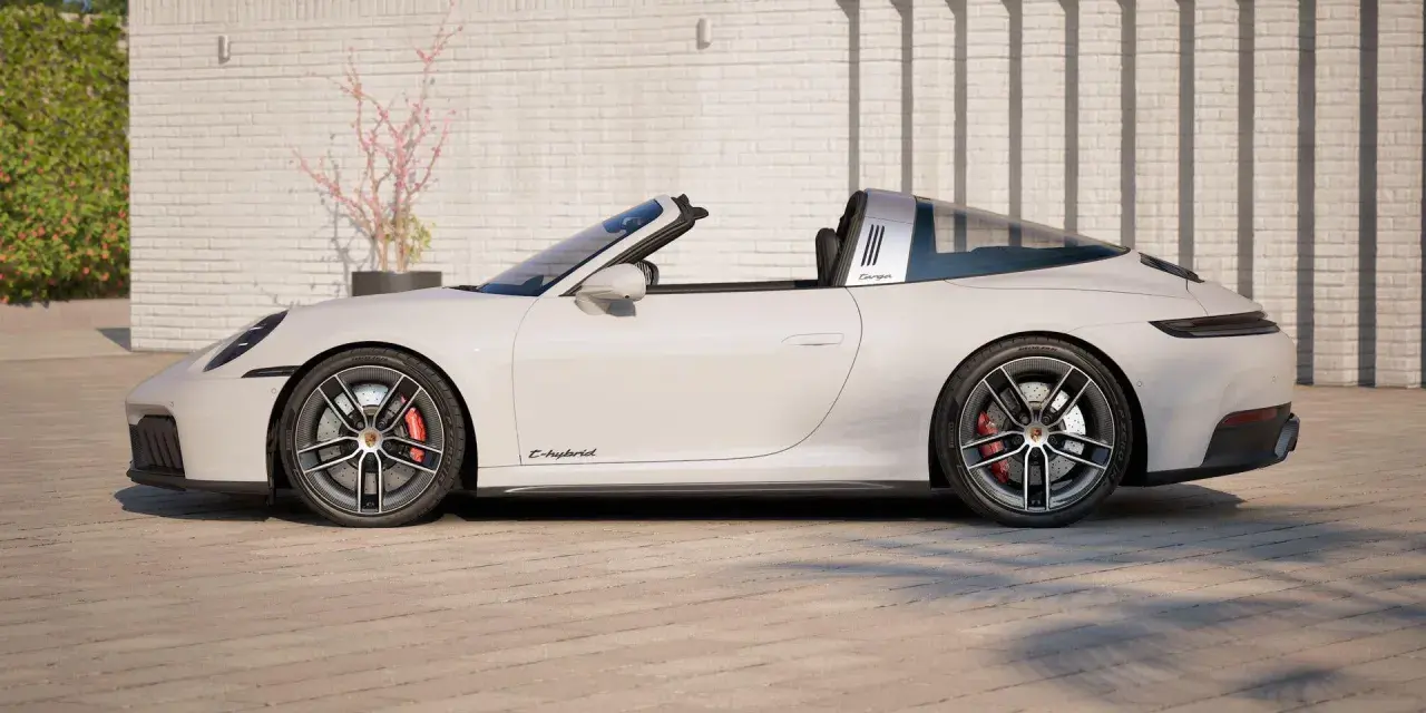 Białe Porsche 911 Targa z napisem "E-hybrid" na progu, zaparkowane przed ceglanym murem.
