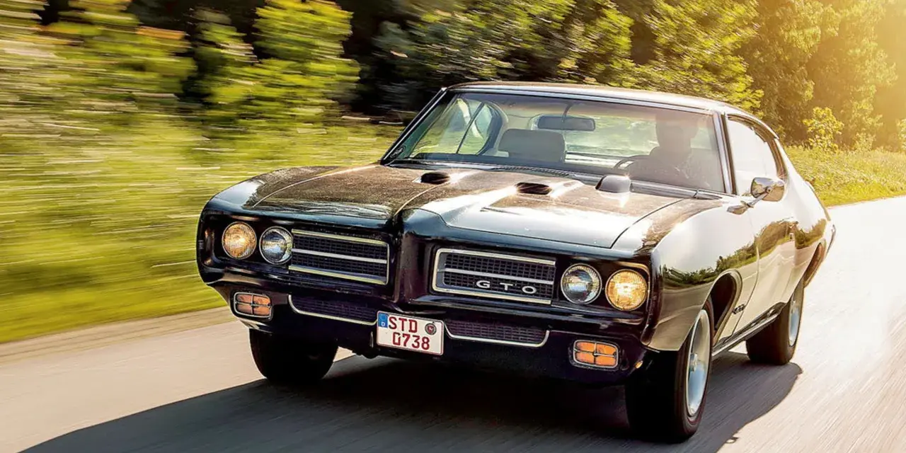 Czarny Pontiac GTO mknie po drodze, otoczony zielenią.
