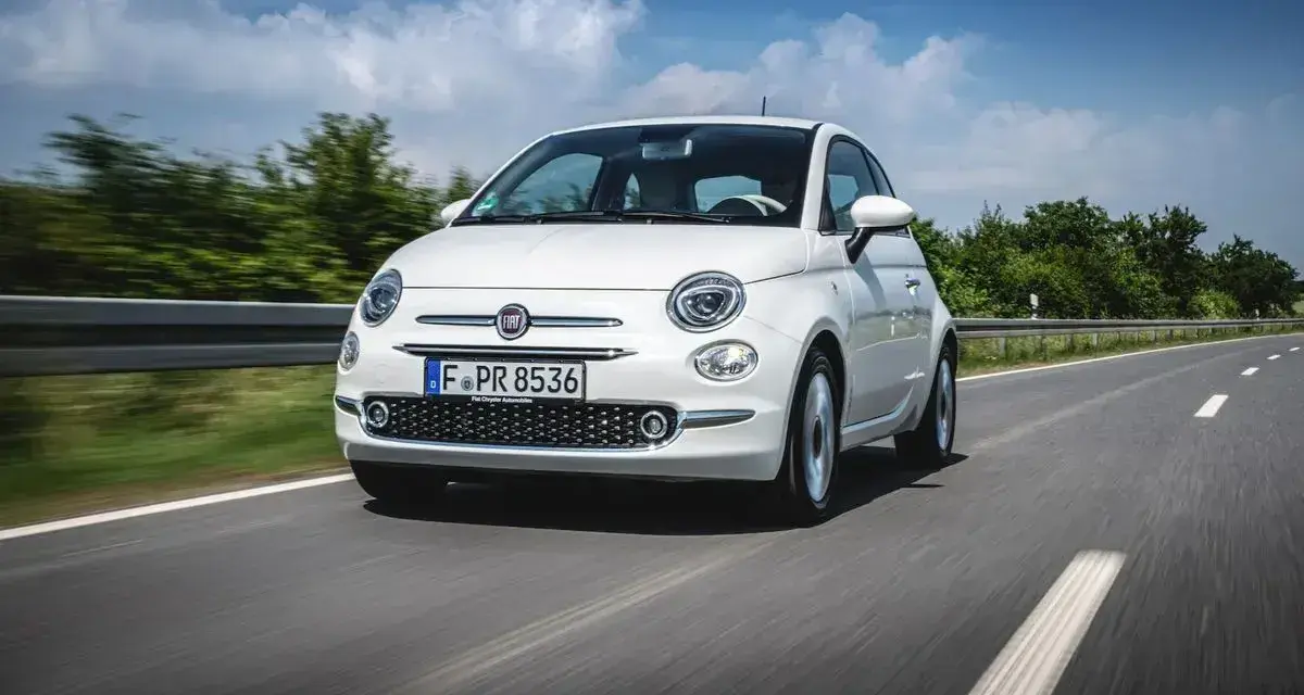 Biały Fiat Panda 3 jedzie po drodze, otoczony zielenią i błękitnym niebem.