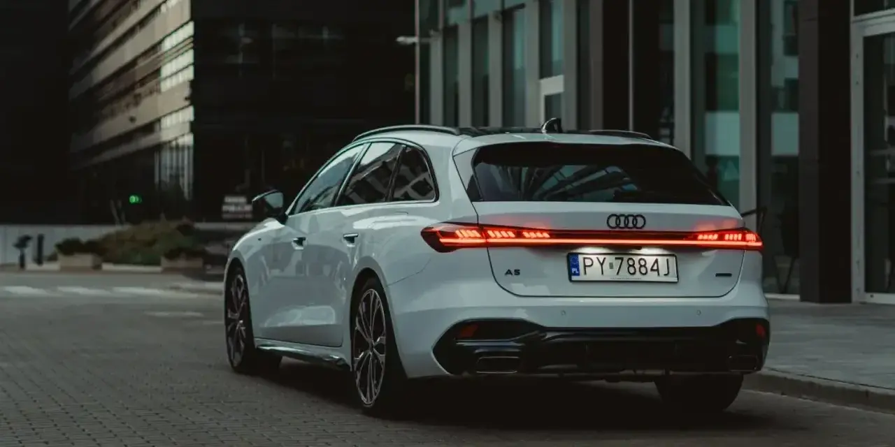 Białe Audi A5 Avant z nowoczesnymi światłami LED na tle miejskiej architektury.