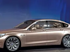 Eleganckie, złote bmw gt z przyciemnianymi szybami i chromowanymi felgami stoi na tle niebieskiej ściany.