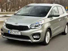 Srebrny Kia Carens, typowy MPV, jedzie po drodze. To auto rodzinne, idealne na wycieczki.