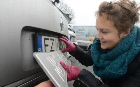 Kobieta w czerwonych rękawiczkach montuje tablicę rejestracyjną.