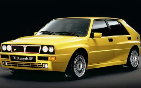 Żółta Lancia Delta Integrale HF z lat 90. na czarnym tle, z charakterystycznym grillem i felgami.