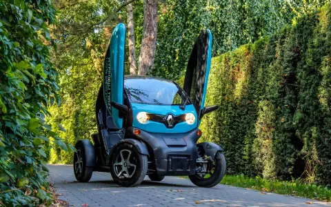 Niebieski Renault Twizy z otwartymi drzwiami stoi na ścieżce wśród zieleni.
