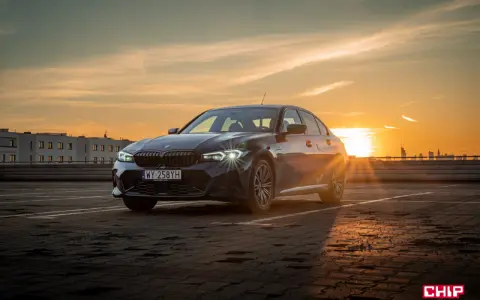 Ciemnoszara limuzyna BMW 330e na parkingu o zachodzie słońca.