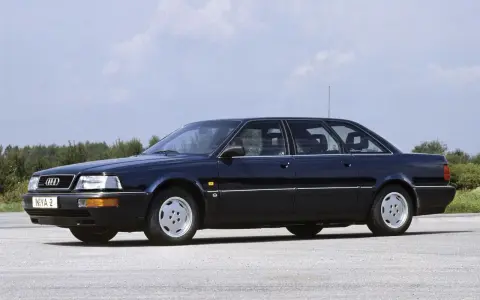 Ciemnoniebieski Audi V8 z lat 90. stoi na pustej drodze, z drzewami w tle.