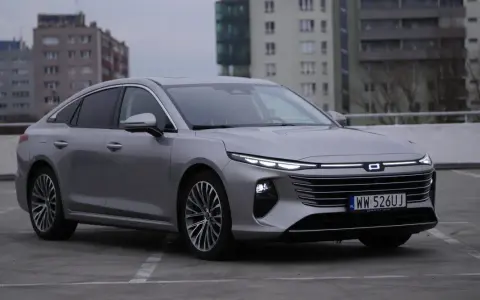 Srebrny Bestune B70 z nowoczesnymi światłami LED zaparkowany na betonowym placu, w tle budynki mieszkalne.