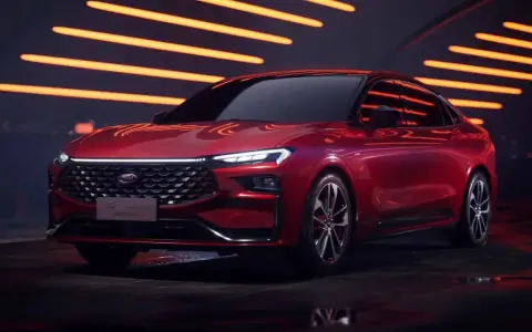 Czerwony Ford Mondeo MK6 z nowoczesnym designem, błyszczącym grillem i ostrymi światłami LED, prezentowany na tle pomarańczowych świateł.