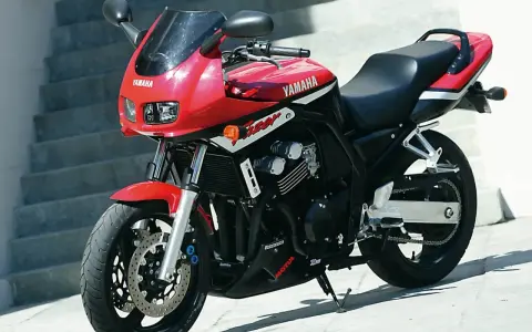 Czerwony motocykl Yamaha FZ6 z czarnym siedzeniem i owiewką, zaparkowany na zewnątrz.