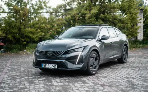 Nowy Peugeot 408 w ciemnoszarym kolorze prezentuje się elegancko na tle zieleni.