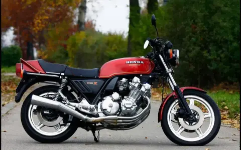Klasyczny czerwony motocykl Honda CBX 1000 z lat 80. stoi na drodze, otoczony jesienną zielenią i opadłymi liśćmi.