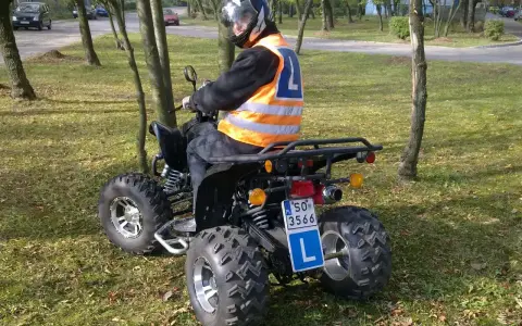 Mężczyzna w kasku i kamizelce odblaskowej siedzi na quadzie z literą L. Zastanawiasz się, jakie prawo jazdy na quada jest potrzebne?