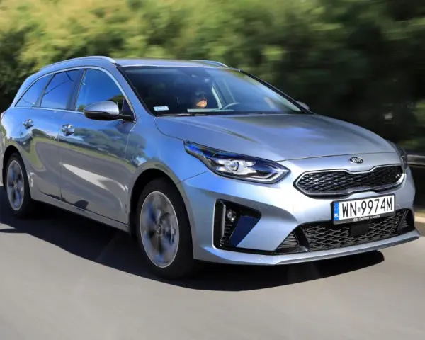 Srebrny Kia Ceed 1.6 benzyna w wersji kombi pędzi po drodze, otoczony zielenią.