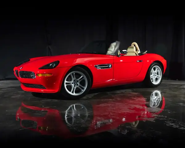 Czerwony kabriolet BMW Z8 z beżowym wnętrzem, lśniący na mokrej podłodze, odbija się w tafli wody.