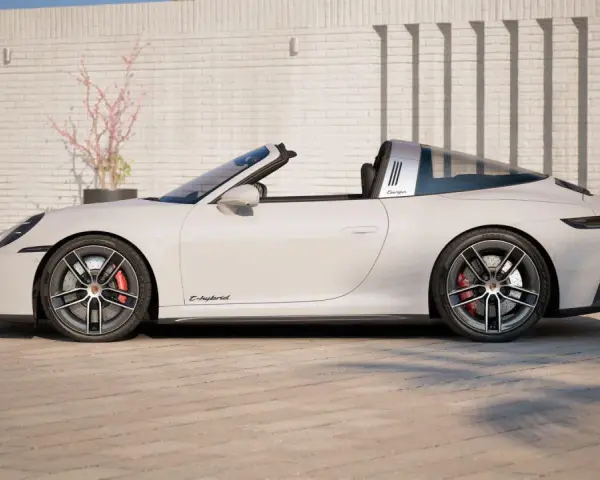 Białe Porsche 911 Targa z napisem "E-hybrid" na progu, zaparkowane przed ceglanym murem.