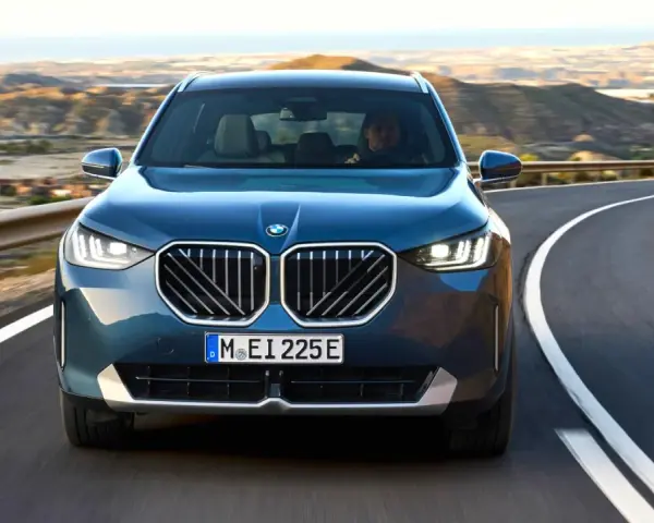 Nowy **BMW X3 2025** w kolorze granatowym jedzie krętą drogą pośród pustynnych krajobrazów.