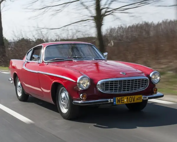 Czerwone Volvo P1800 sunie po drodze, otoczone drzewami. Klasyk z lat 60. w pełnej krasie.