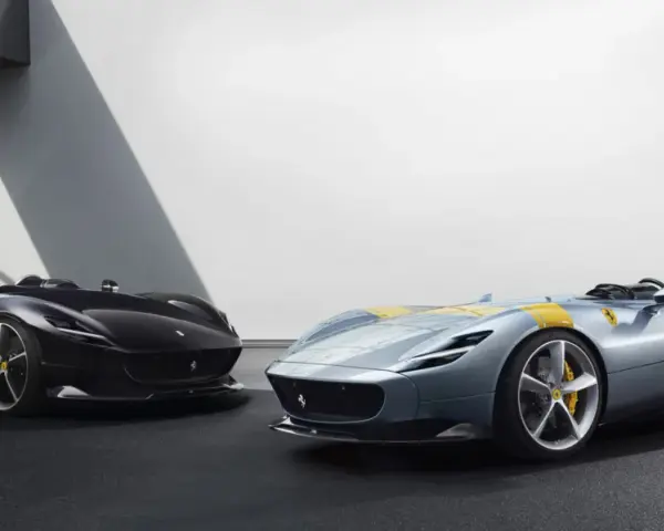 Dwa sportowe samochody Ferrari Monza SP2, jeden czarny, drugi błękitny z żółtymi pasami, prezentują swoje aerodynamiczne kształty.