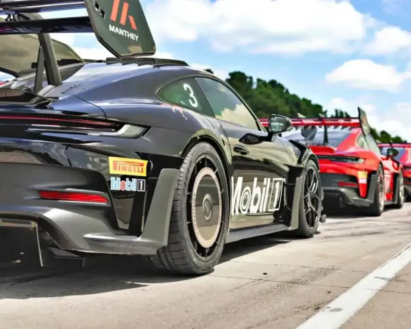 Czarny Porsche GT3 RS z numerem 3 i logo Manthey na skrzydle, gotowy do wyścigu obok czerwonych samochodów.
