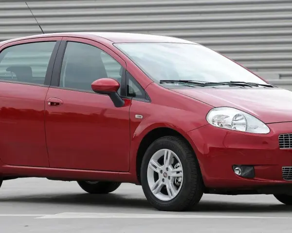 Czerwony Fiat Punto Evo z polskimi tablicami SB 2823E zaparkowany na szarym podłożu, z metalową ścianą w tle.