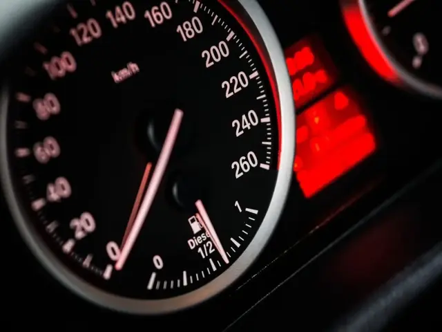Zbliżenie na deskę rozdzielczą samochodu: prędkościomierz pokazuje 80 km/h, a obok wskaźnik paliwa jest na 1/2. Widoczny jest również licznik spalania paliwa.