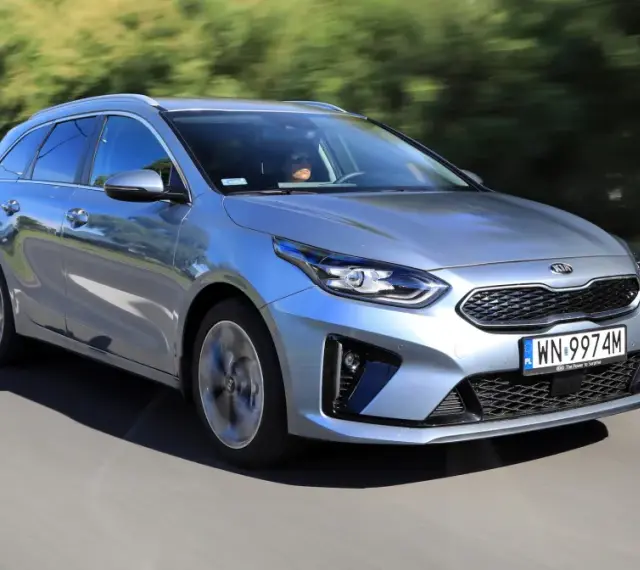 Srebrny Kia Ceed 1.6 benzyna w wersji kombi pędzi po drodze, otoczony zielenią.