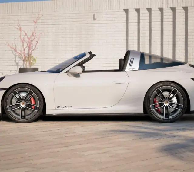 Białe Porsche 911 Targa z napisem "E-hybrid" na progu, zaparkowane przed ceglanym murem.