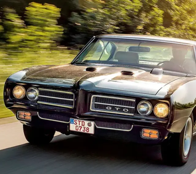 Czarny Pontiac GTO mknie po drodze, otoczony zielenią.