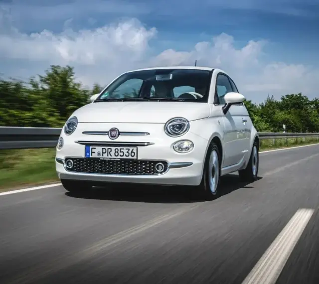Biały Fiat Panda 3 jedzie po drodze, otoczony zielenią i błękitnym niebem.