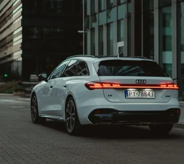 Białe Audi A5 Avant z nowoczesnymi światłami LED na tle miejskiej architektury.