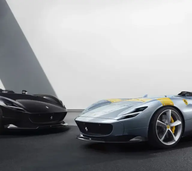 Dwa sportowe samochody Ferrari Monza SP2, jeden czarny, drugi błękitny z żółtymi pasami, prezentują swoje aerodynamiczne kształty.