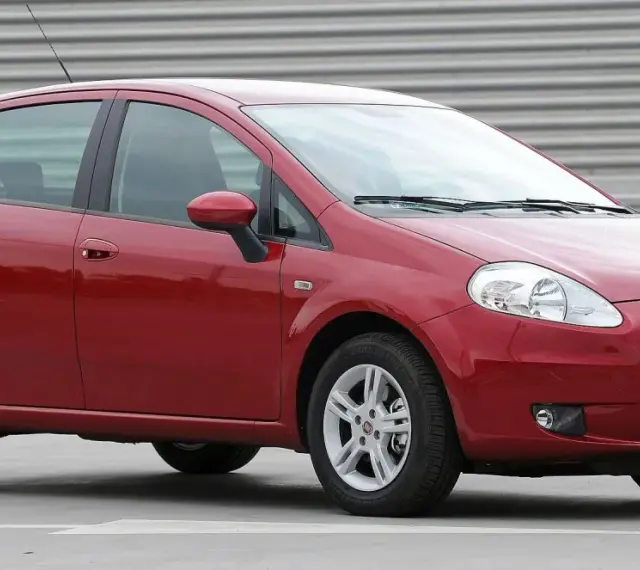 Czerwony Fiat Punto Evo z polskimi tablicami SB 2823E zaparkowany na szarym podłożu, z metalową ścianą w tle.