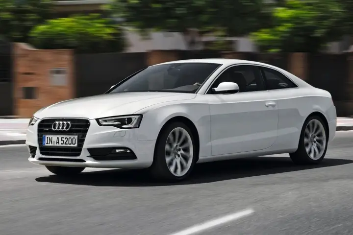 Białe Audi A5 Coupe pędzi po drodze, jego sylwetka jest dynamiczna i elegancka.