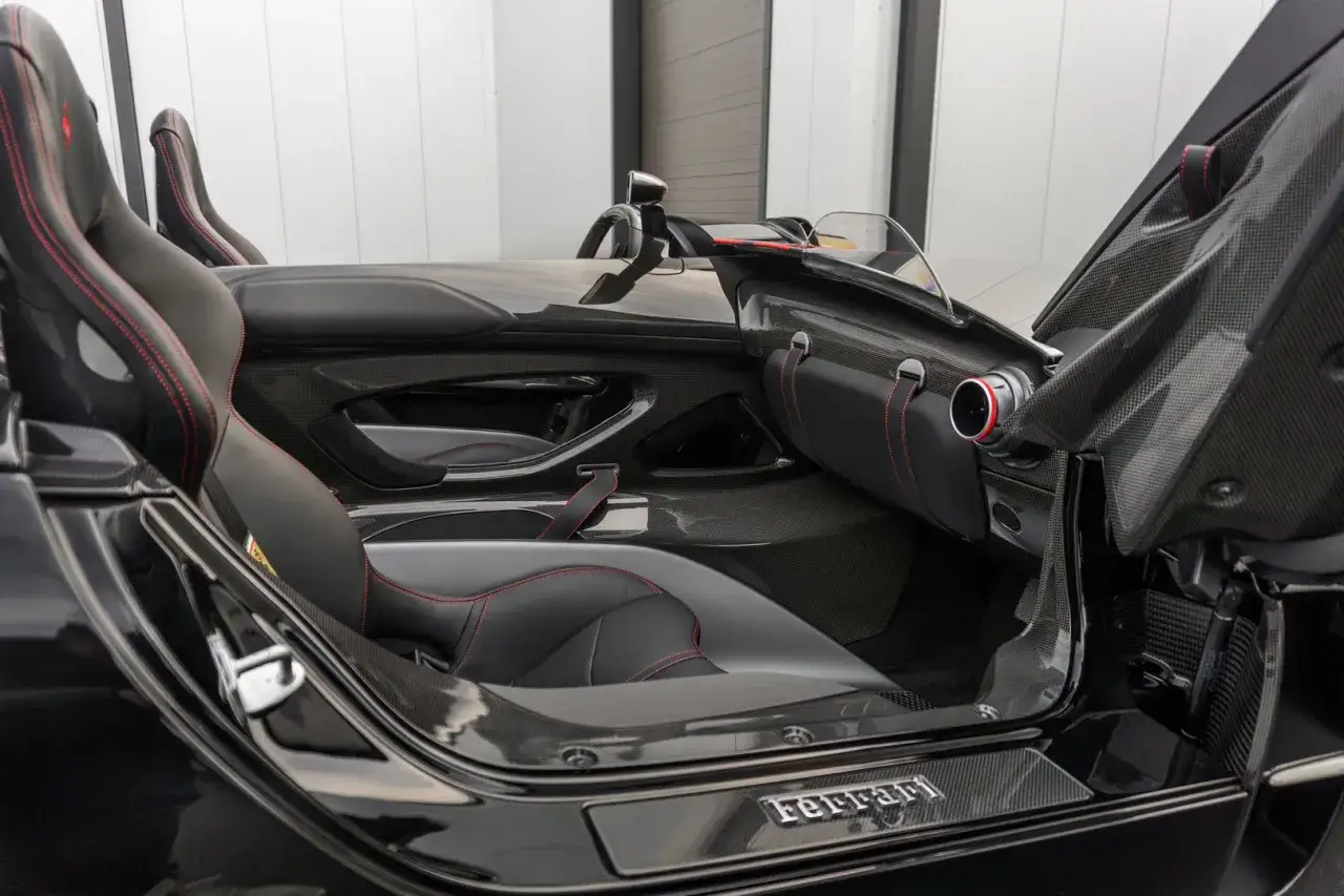 Wnętrze Ferrari Monza SP2 z czarną tapicerką i czerwonymi przeszyciami. Widoczne sportowe fotele i elementy z włókna węglowego.