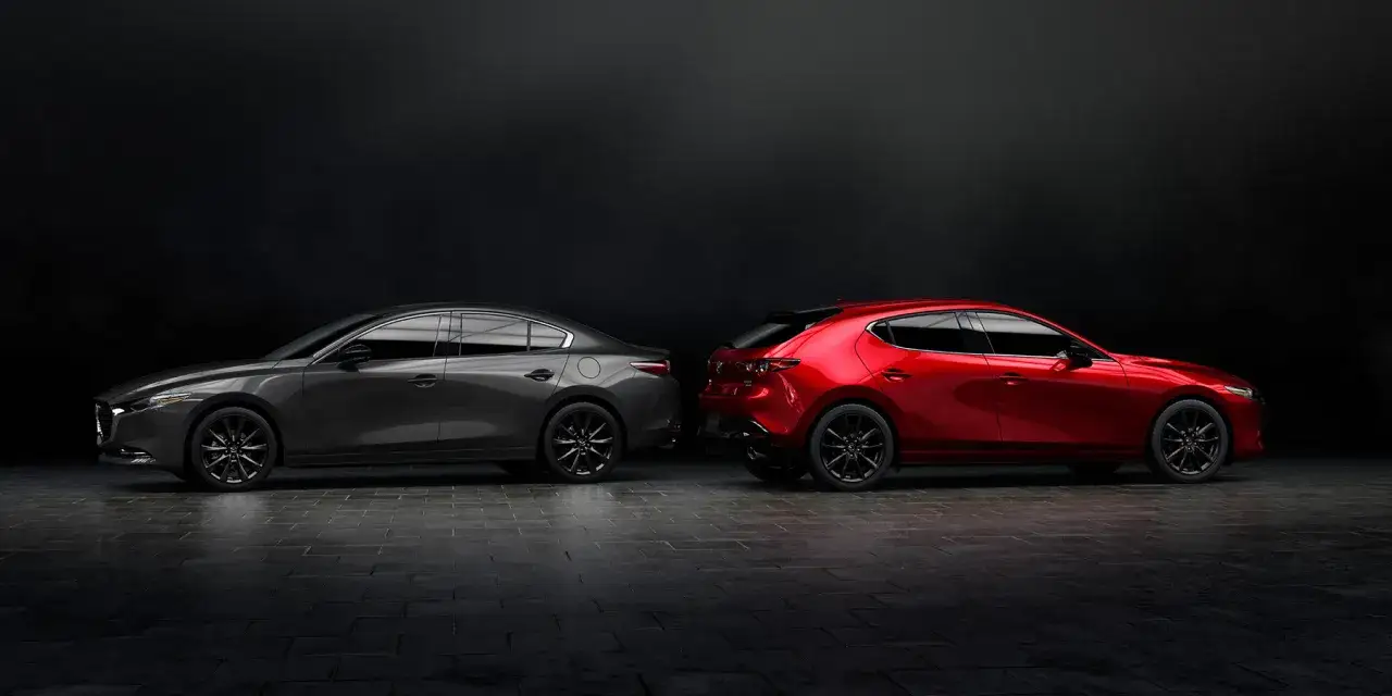 Dwa samochody: szary sedan i czerwony liftback, stojące obok siebie na ciemnym tle.