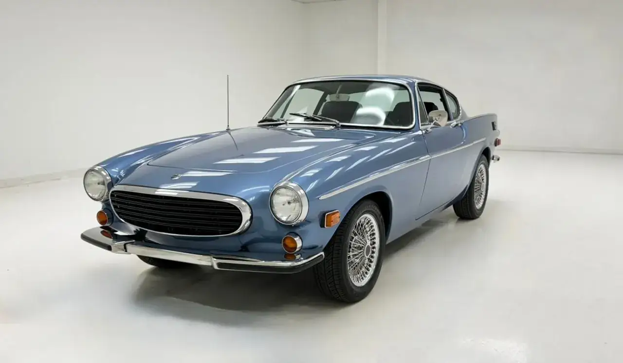 Niebieskie Volvo P1800 z lat 70. z chromowanymi felgami i grillem, prezentujące klasyczny styl coupe.