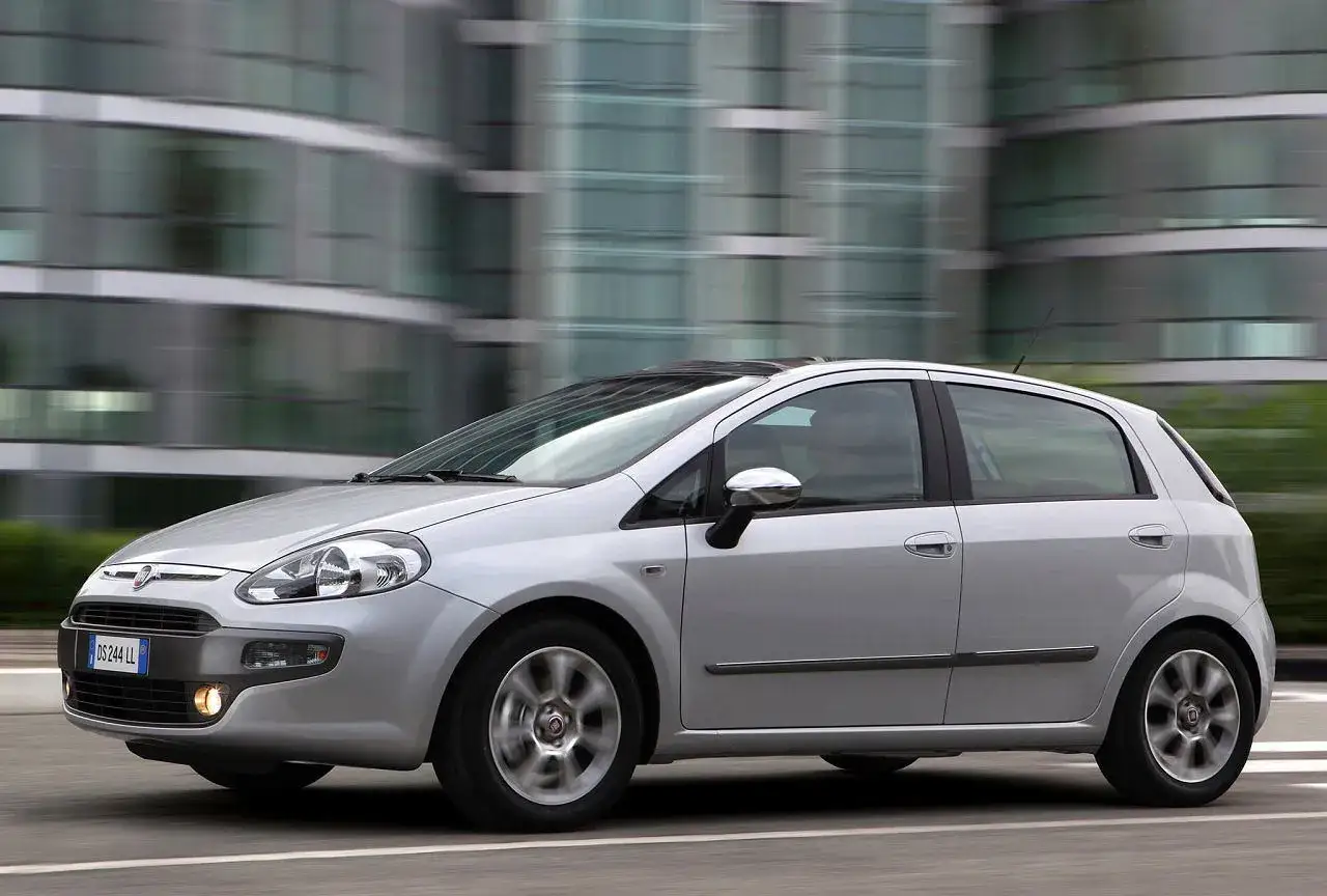 Srebrny Fiat Punto Evo pędzi ulicą, mijając nowoczesne budynki.