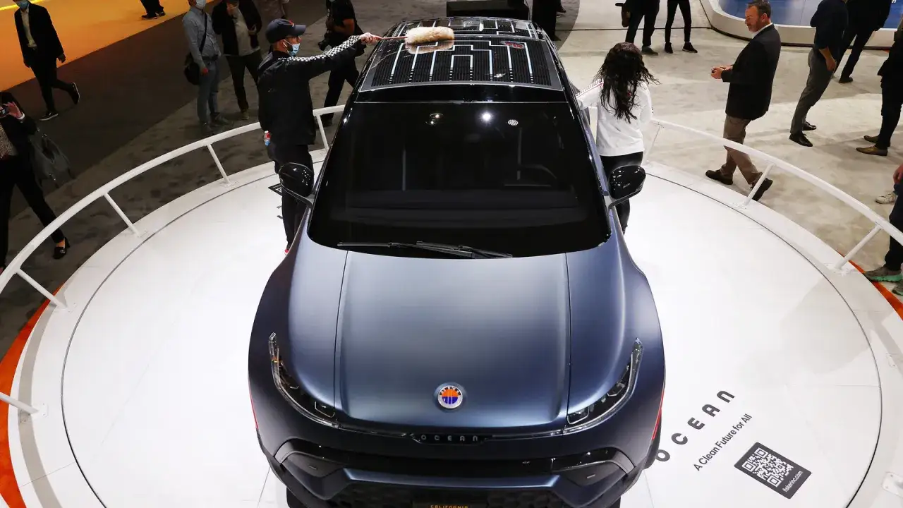 Mężczyzna czyści dach Fisker Karma, który ma panele słoneczne. Samochód stoi na wystawie, otoczony ludźmi.